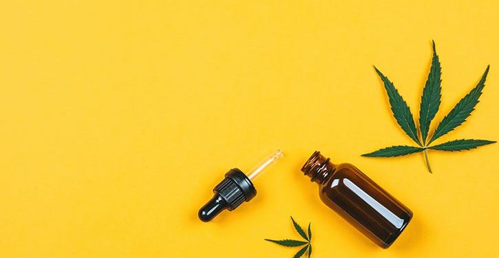 Cannabis leaf and cbd oil on a yellow backdrop